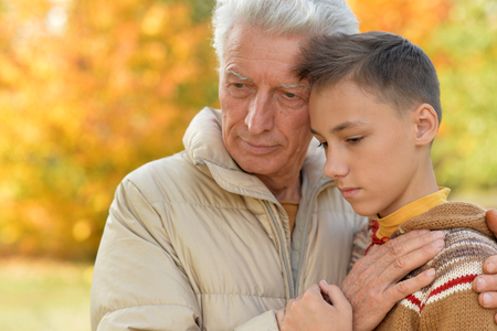 Portrait of sad grandfather and grandson hugging in parkの写真素材