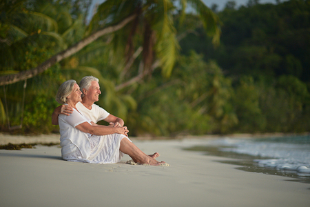 Portrait of happy elderly couple sitting on tropical beachの写真素材