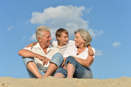 Portrait of boy with grandparents relaxing on sandy beachの写真素材