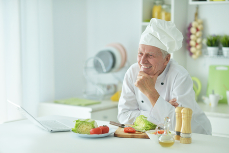 Portrait of elderly male chef cooking at table with laptopの写真素材