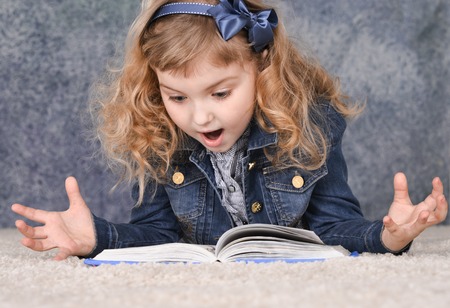Cute little girl reading book while lying on floor