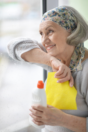 Portrait of senior beautiful woman posing and cleaning window at homeの写真素材