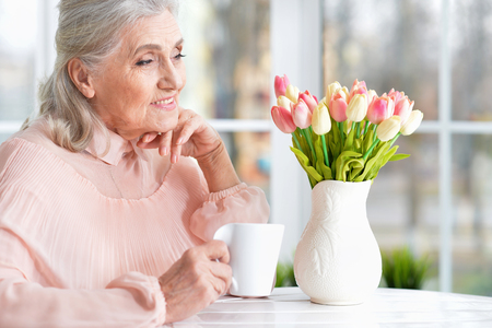 Beautiful senior woman drinking tea while sitting at tableの写真素材