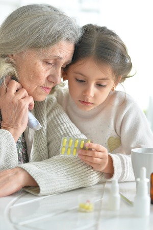 Cute girl giving medicine to sick senior womanの写真素材