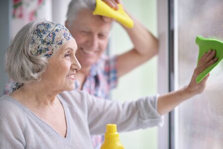 Portrait of happy senior couple cleaning window at homeの写真素材
