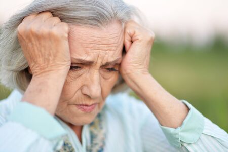 Senior beautiful woman with headache in spring park