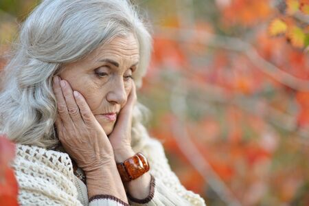 Portrait of sad senior woman in autumn park