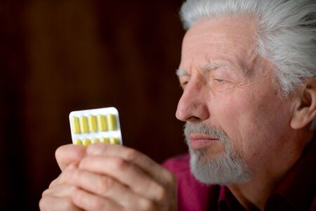 Portrait of sad sick senior man with pills