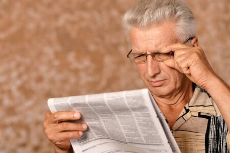 Close-up portrait of senior man reading newspaper on a beige background