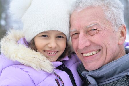 Close up portrait of grandfather with granddaughter smiling, posing outdoors in winterの写真素材
