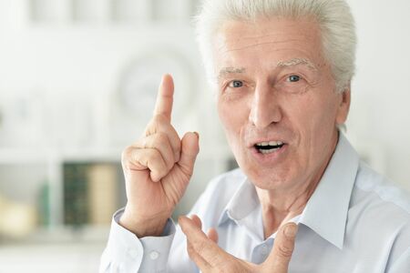 Smiling senior man pointing up with finger at home