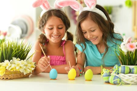 Sisters wearing rabbit ears decorating Easter eggs at home