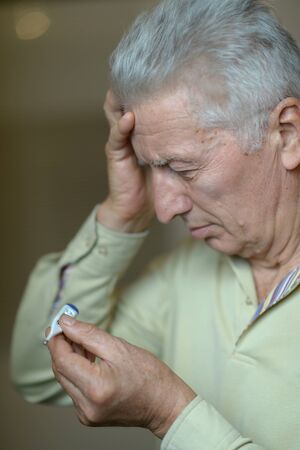 Portrait of sad sick senior man with thermometerの写真素材