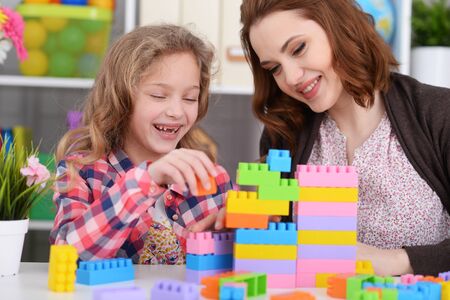 Cute little girl and her mother playing colorful plastic blocksの写真素材