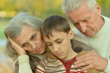 Sad grandfather, grandmother and grandson hugging in parkの写真素材
