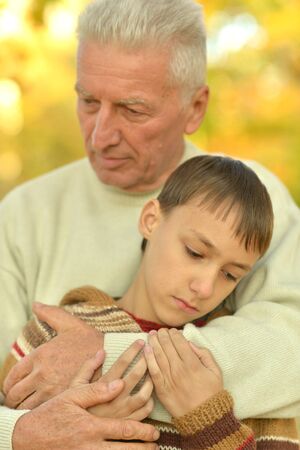Sad grandfather and grandson hugging in parkの写真素材