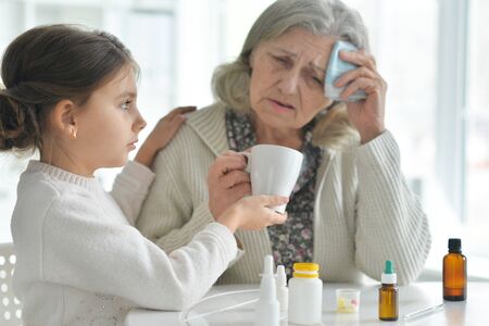 Cute girl giving medicine to sick senior womanの写真素材