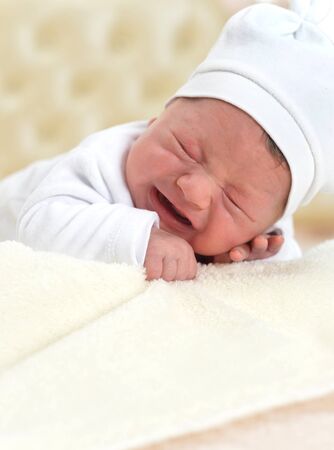 Portrait of crying little baby boy on bedの写真素材