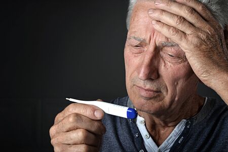 Portrait of sick senior man with thermometer at home