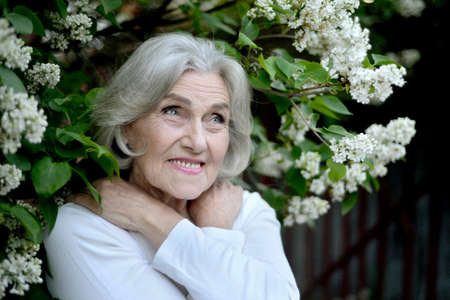 Happy senior beautiful woman with lilacs in spring parkの写真素材