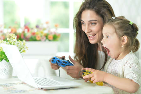Emotional happy mother and daughter using laptop playing video game