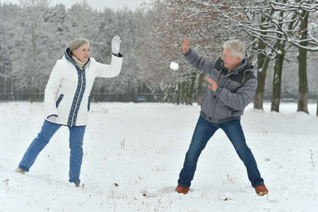 Happy senior couple at snowy winter park playing snowballs