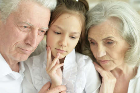 Sad grandmother, grandfather and granddaughter hugging at home