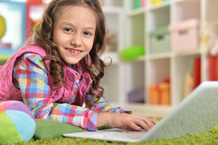 Cute girl using laptop while lying on green floorの写真素材