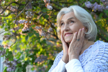 Senior beautiful happy woman posing by lilacs in parkの写真素材