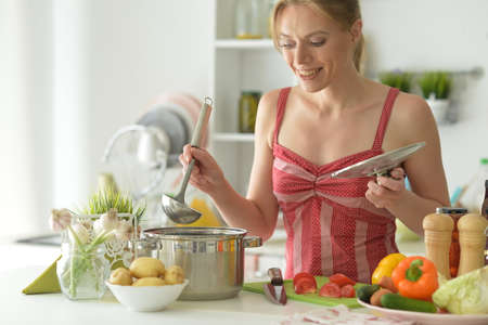 Beautiful young woman cooking soup in kitchen