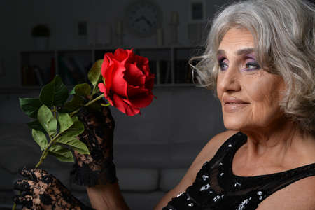 Beautiful senior woman with red rose isolated on black backgroundの写真素材