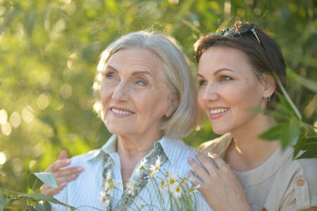 Smiling senior woman with adult daughter with flowers in park