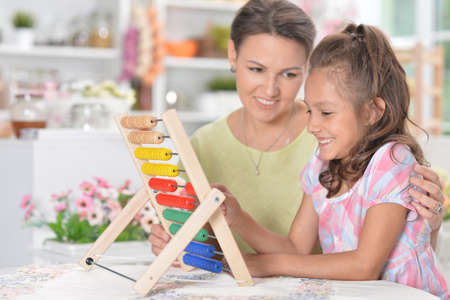 Mother teaching her daughter to use abacus indoorsの写真素材