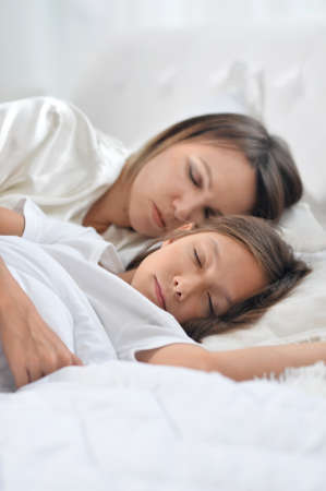 Cute girl and her mother sleeping in her bedの写真素材