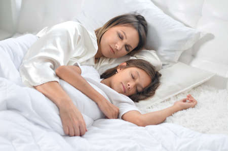 Cute girl and her mother sleeping in her bedの写真素材