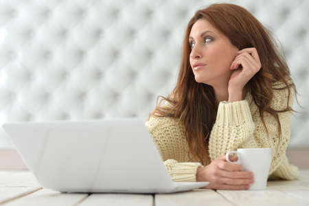 Beautiful young woman with laptop sitting on floor and drinking coffee