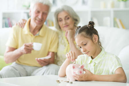 Happy grandparents and grandchild with piggy bank at homeの写真素材
