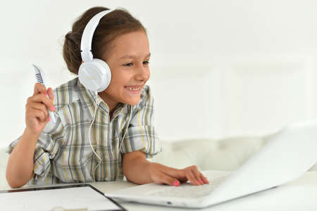 Cute girl in headphones using laptop at home at desk