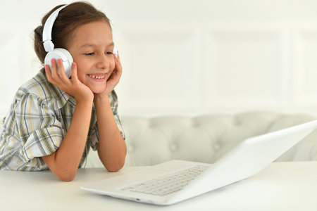 Cute girl in headphones using laptop at home at deskの写真素材
