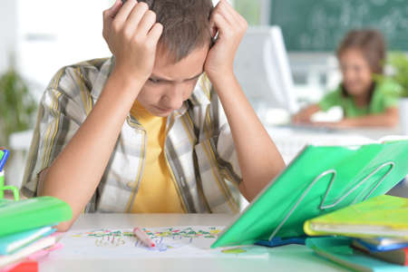 Tired boy sitting at table and studying at home