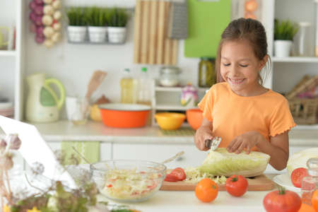 Cute girl making salad on kitchen and using laptopの写真素材