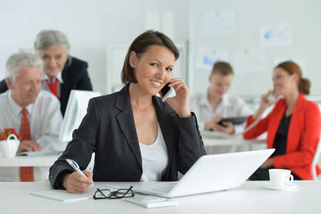Woman with smartphone and a laptop in officeの写真素材