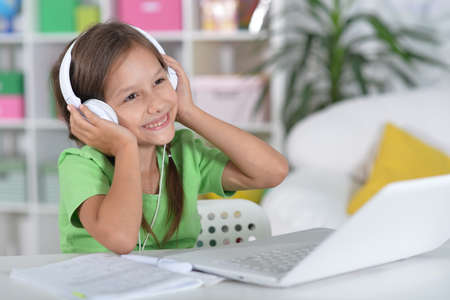 Cute girl in headphones using laptop at home at desk
