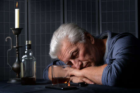Caucasian senior man with bottle of alcohol sleeping on tableの写真素材