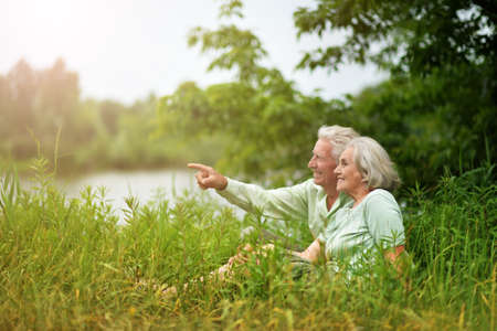 Happy senior couple in summer park. man pointing with fingerの写真素材