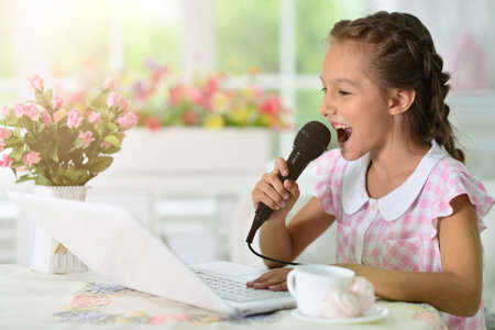 Portrait of little girl with laptop singing karaokeの写真素材