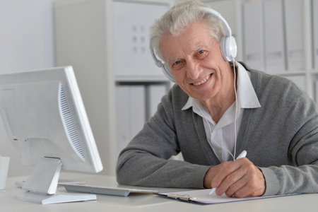 Elderly man in headphones take online course on computer at home.の写真素材