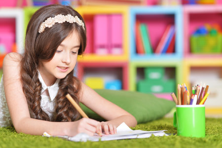 Beautiful little girl draws with a pencil on a sheet of paperの写真素材