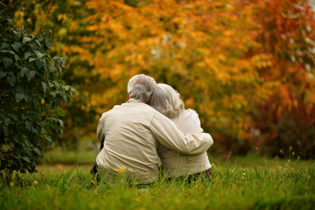 Elderly couple sits in a park on the grass in autumn. back view.の写真素材