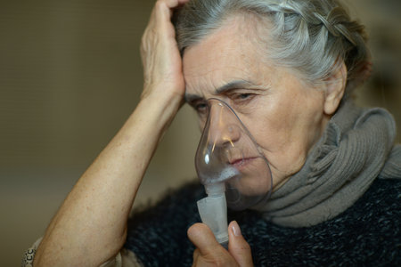 Beautiful elderly woman sits with a mug of tea on the background of the window in winterの写真素材